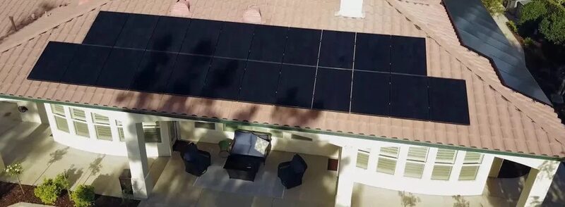 Aerial view of black solar panels installed on the tiled roof of a house with a patio below