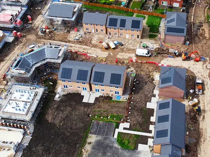 Aerial view of a new-build housing development with roof-integrated solar panels on several homes under construction