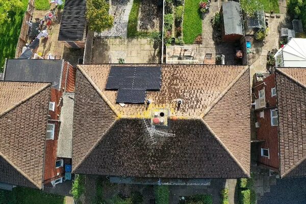 An aerial view of a terracotta-tiled house roof with a small array of black solar panels, surrounded by neighbouring roofs and gardens