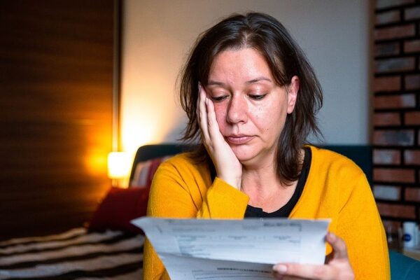 A worried woman in a yellow cardigan at home reading a paper bill or letter