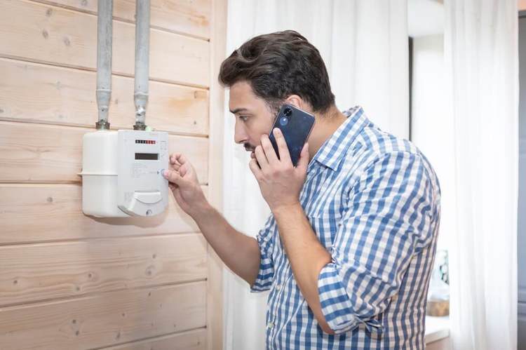 A man on a mobile phone reading a wall-mounted gas meter in a home