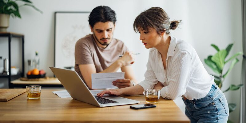 A couple at a kitchen table reviewing a paper bill together while using a laptop