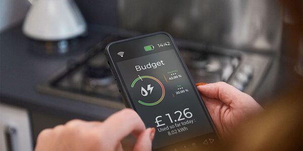 A person holding a smartphone showing an energy budget app screen with £1.26 used so far, in a kitchen