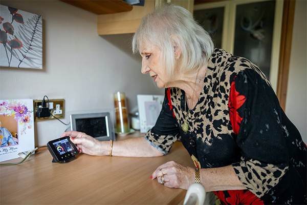 An older woman at home checking a smart meter display on a kitchen counter
