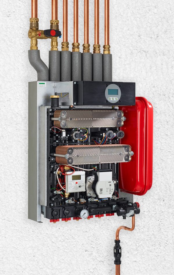 A wall-mounted heat network heating interface unit (HIU) with copper pipework, plate heat exchangers, valves and a red expansion vessel