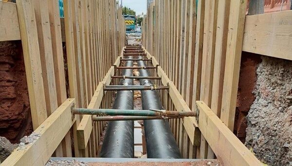 District heat network pipes being installed in a timber-shored trench at a street works site