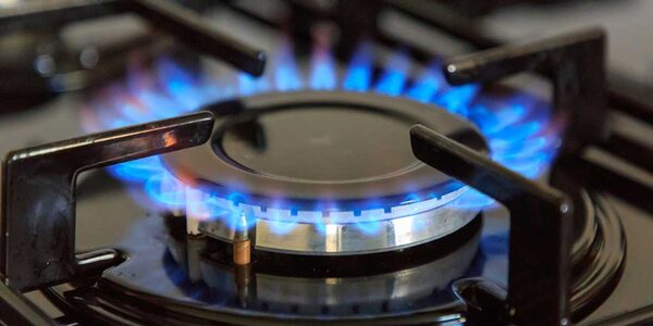 A lit gas hob burner with blue flames on a black gas cooker