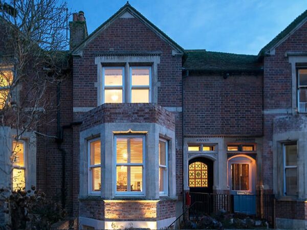 A brick Victorian terraced house at dusk with warmly lit sash and bay windows, photographed from the street