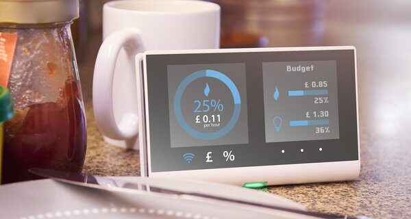 A smart energy monitor on a kitchen worktop displaying live energy cost per hour and budget figures