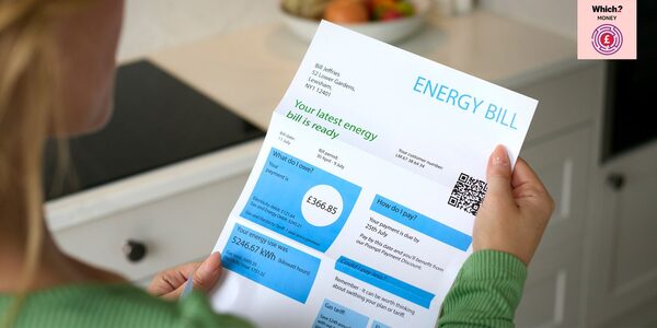 A woman reading a paper energy bill showing amounts owed and electricity usage in a kitchen