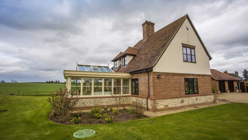 A large brick country house with a conservatory and a green buried LPG tank access cover in the lawn