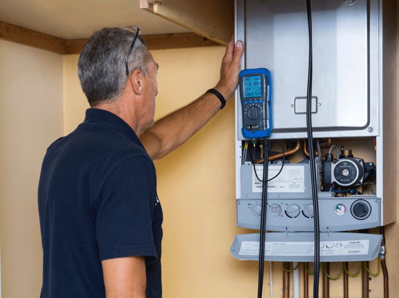 A technician using a blue flue gas analyser to test a wall-mounted domestic gas boiler with its casing removed