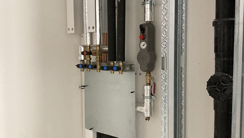 A heat network HIU (heat interface unit) with insulated pipes, valves and pressure gauge installed in a plant cupboard