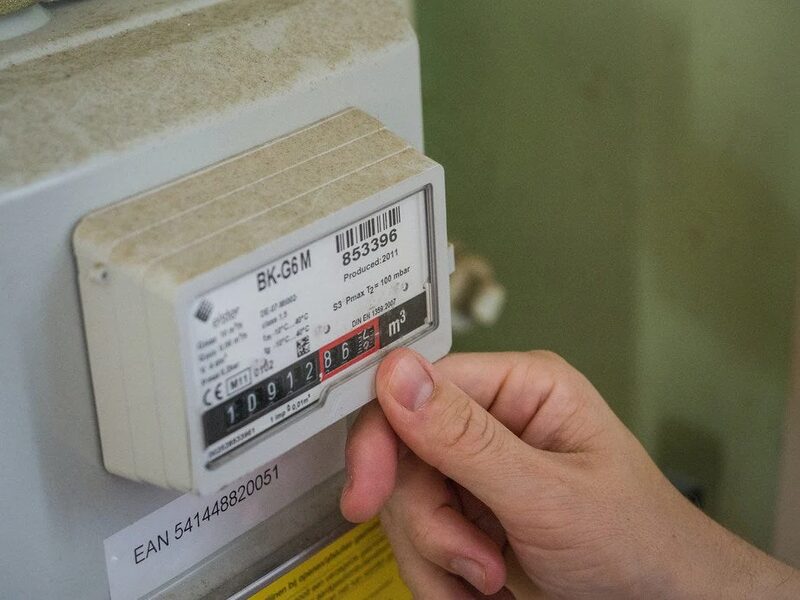 A hand reading a BK-G6M Elster gas meter mounted on a wall