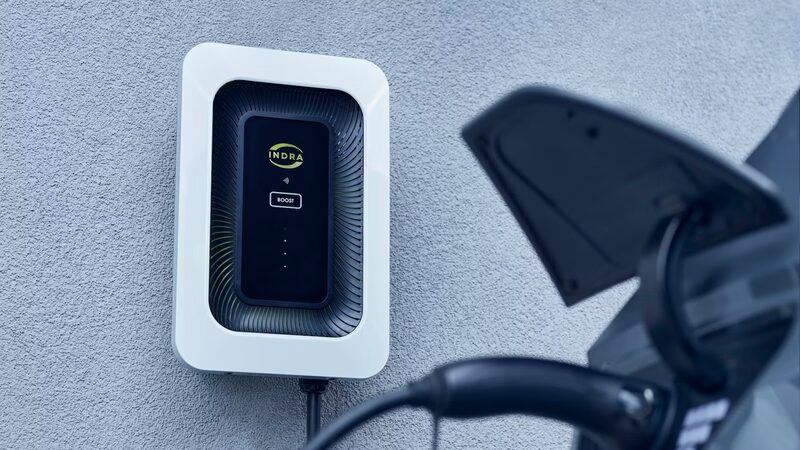 An Indra wall-mounted home EV charger with a charging cable plugged into a car