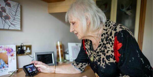 An older woman at home checking a smart meter display on a shelf