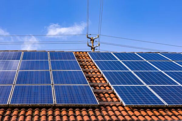 Blue polycrystalline solar panels installed on a terracotta-tiled roof under a blue sky with power lines behind