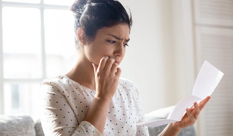A woman at home looking anxiously at a paper bill or letter