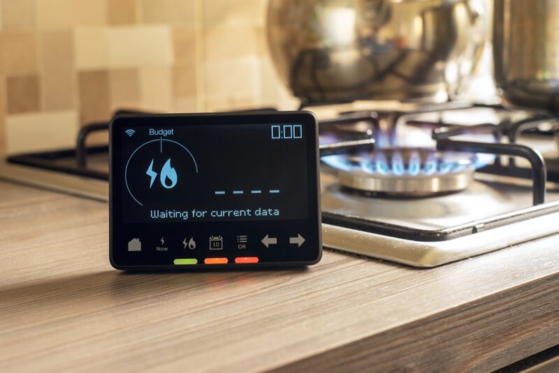 A smart meter display showing 'Waiting for current data' on a kitchen worktop beside a lit gas hob