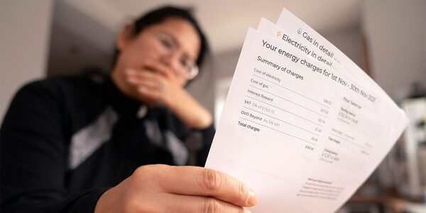 A woman looking worried while holding a household energy bill showing electricity and gas charges