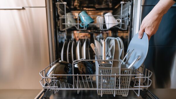 A person loading a plate into an open dishwasher in a kitchen