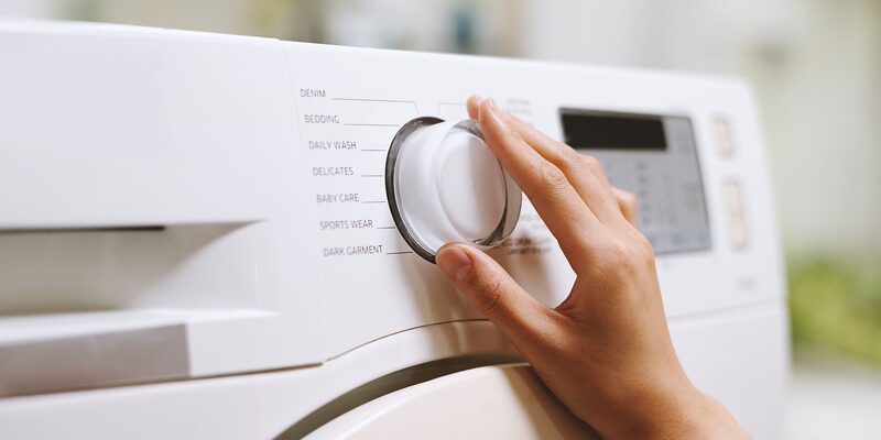 A hand turning the programme dial on a white washing machine