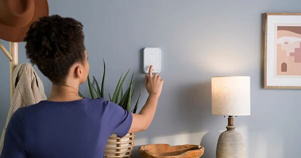 A woman adjusting a white wall-mounted smart thermostat in a living room