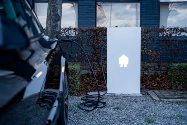 An electric car charging from a white EV charging station outside a dark brick building