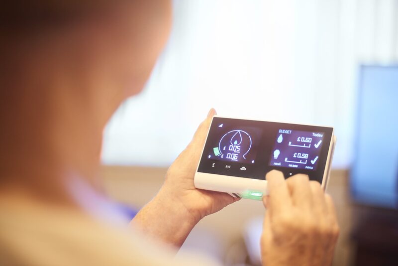 A person holding a smart energy monitor displaying electricity usage and cost figures