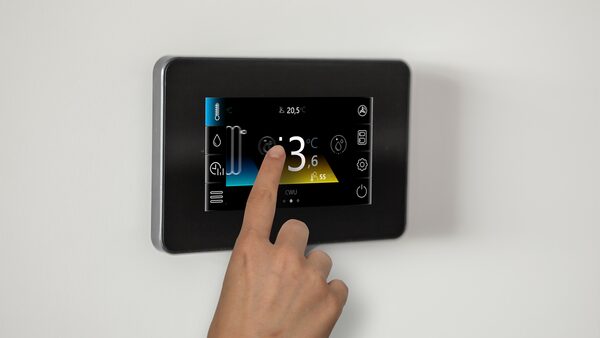 A hand adjusting a wall-mounted Grant heat pump control touchscreen thermostat