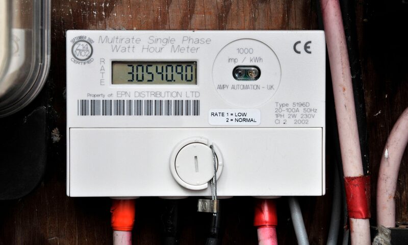 A multirate single-phase electricity meter with digital reading mounted on a wooden wall with cables