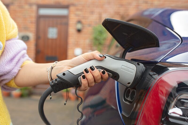 A teal Volkswagen ID.3 electric car charging on the driveway of a modern house at dusk, with a wall-mounted EV charge point on the garage wall