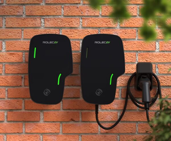 Two black Rolec EV wall-mounted home electric car chargers with green indicator lights on a brick wall, one with a coiled charging cable and socket
