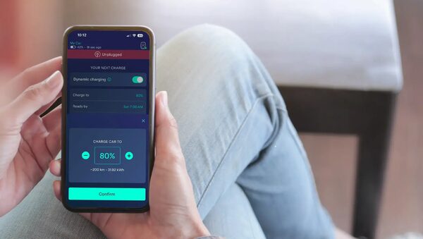 A person holding a smartphone showing the Ohme EV charging app with dynamic charging settings and an 80% charge target