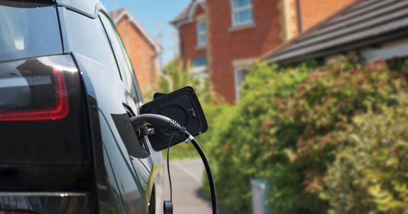 An electric car plugged in with a charging cable on a UK residential driveway