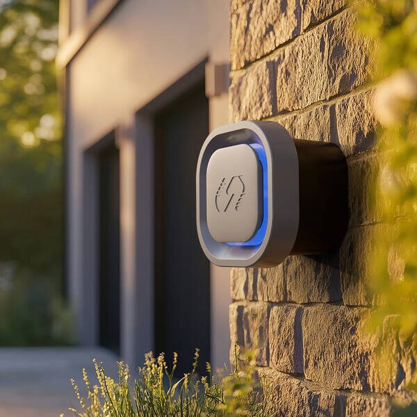 A white wall-mounted EV charger with a blue illuminated ring installed on a stone house exterior wall