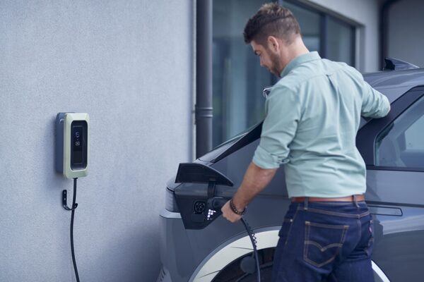 A man plugging a charging cable into an electric car next to a wall-mounted home EV charger