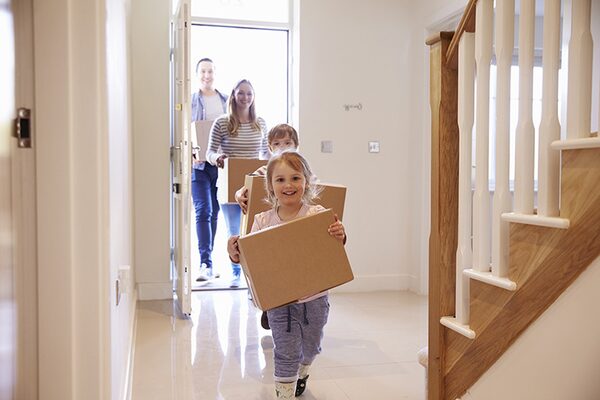 A family carrying cardboard moving boxes into the hallway of a new home