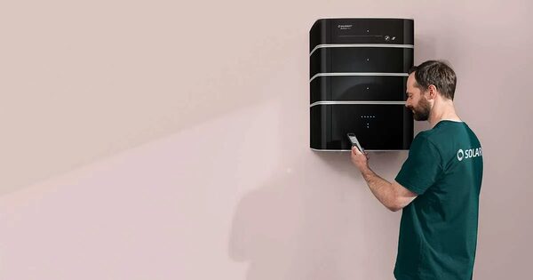 A technician in a Solarwatt t-shirt setting up a wall-mounted Solarwatt battery storage unit