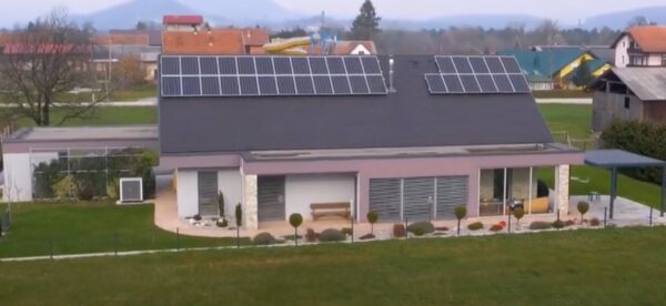 A modern house with solar panels on its large roof, seen from a garden