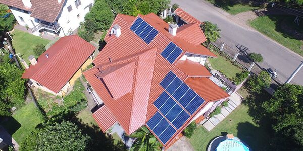 An aerial view of a large house with a red tiled roof fitted with several solar panel arrays