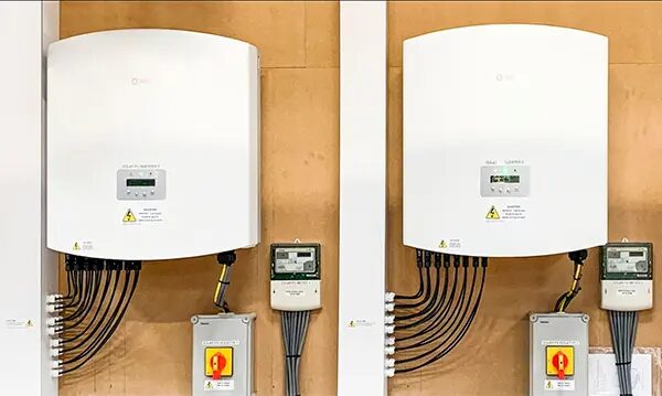 Two white Solis solar inverters mounted on a wall with DC cables, isolator switches and generation meters