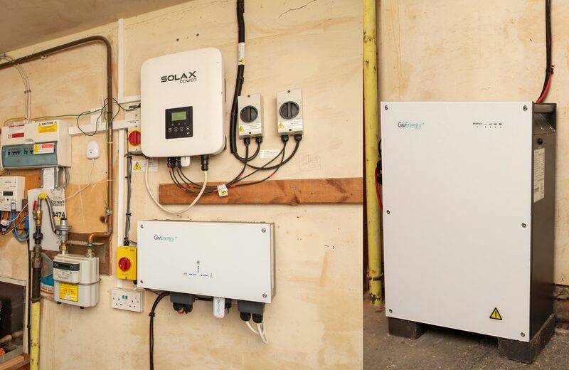 A Solax solar inverter and GivEnergy battery units installed on a garage wall next to a electricity meter and consumer unit