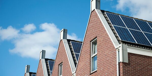 A row of brick houses with solar panels on their roofs under a blue sky