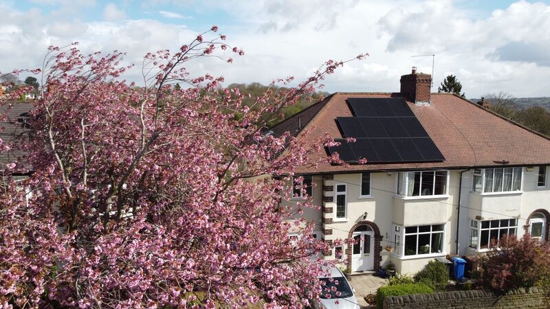 Solar panels on the tiled roof of a UK semi-detached house with a blossoming tree in front