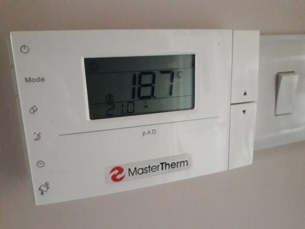 A MasterTherm pAD heat pump controller mounted on a wall showing a room temperature of 18.7°C