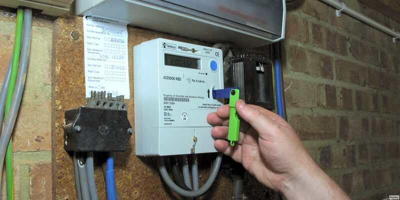 A hand holding a green key being inserted into a Tolka ACE9000KBD prepayment electricity meter mounted on a brick wall