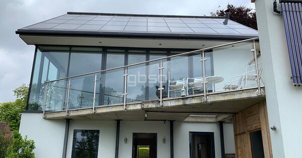 A modern architect-designed house with an in-roof solar panel array on the upper roof and solar thermal tubes on the right wall