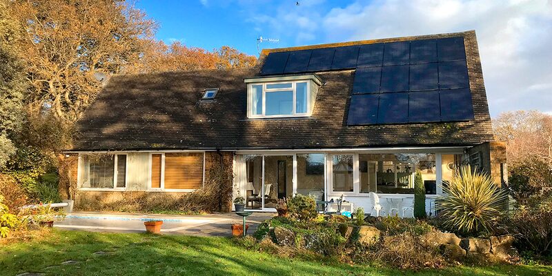 A two-storey house with solar panels on the roof, surrounded by trees and a garden in the foreground