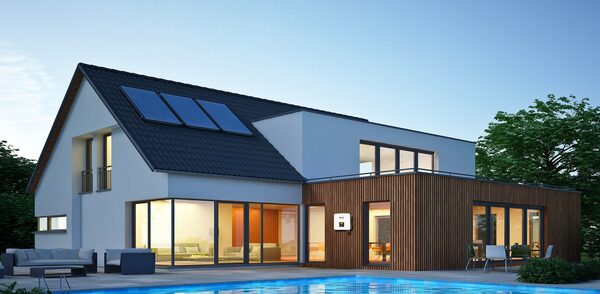 A modern house at dusk with solar panels on the roof and a wall-mounted battery unit on the exterior wall